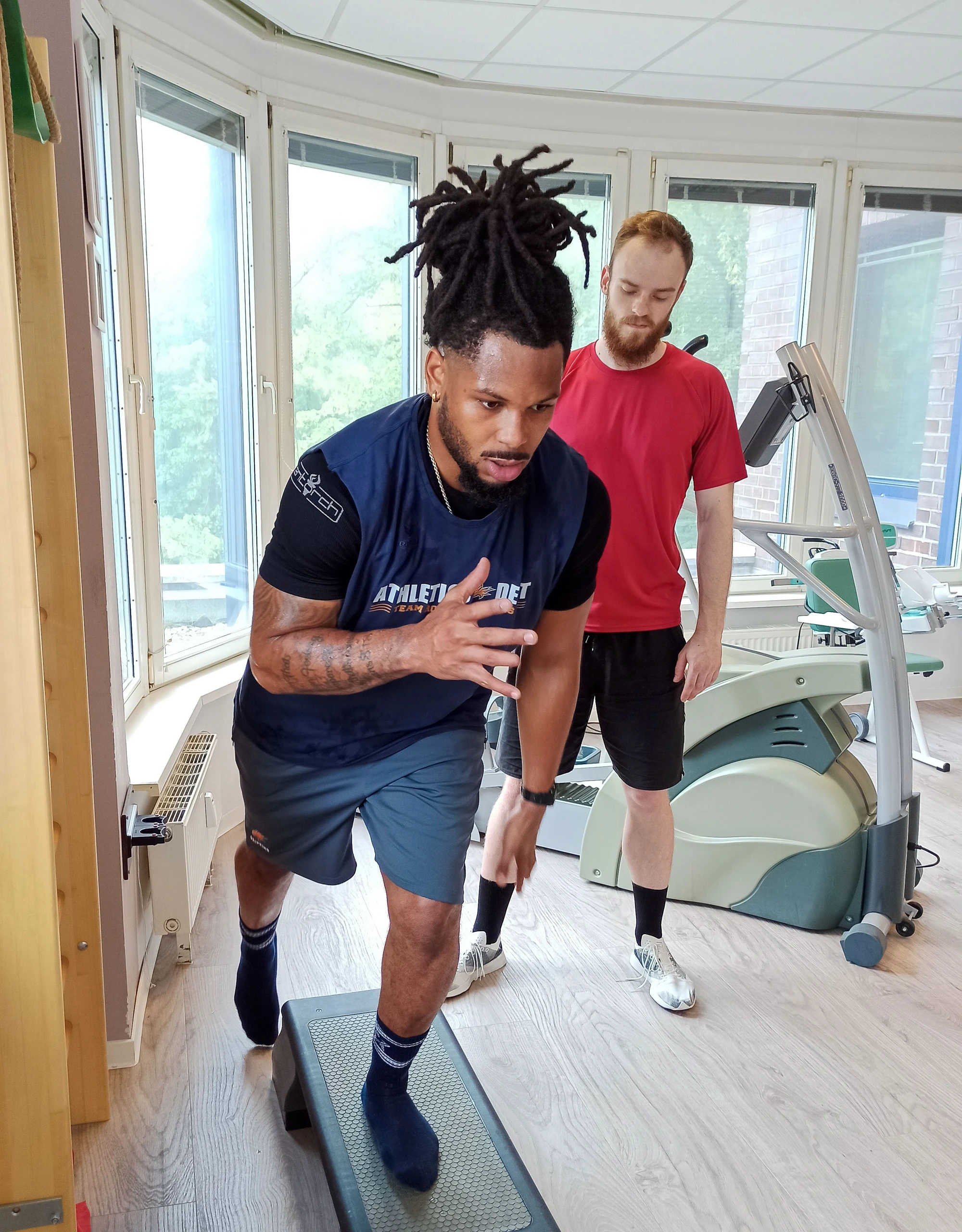 Ein Athlet trainiert auf einer Plattform, während ein Trainer ihn beobachtet und anleitet.