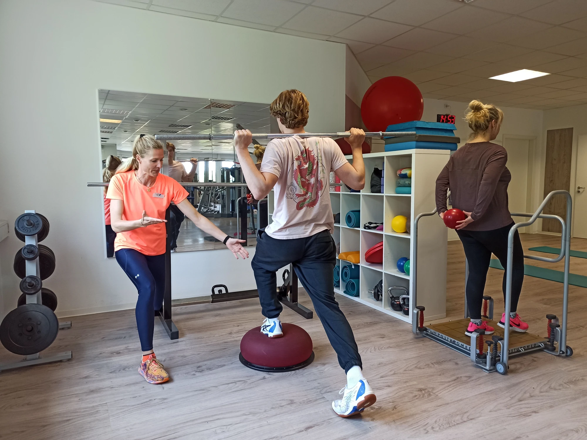 Eine Trainerin gibt Anweisungen, während ein Mann auf einem Balance-Pad trainiert.