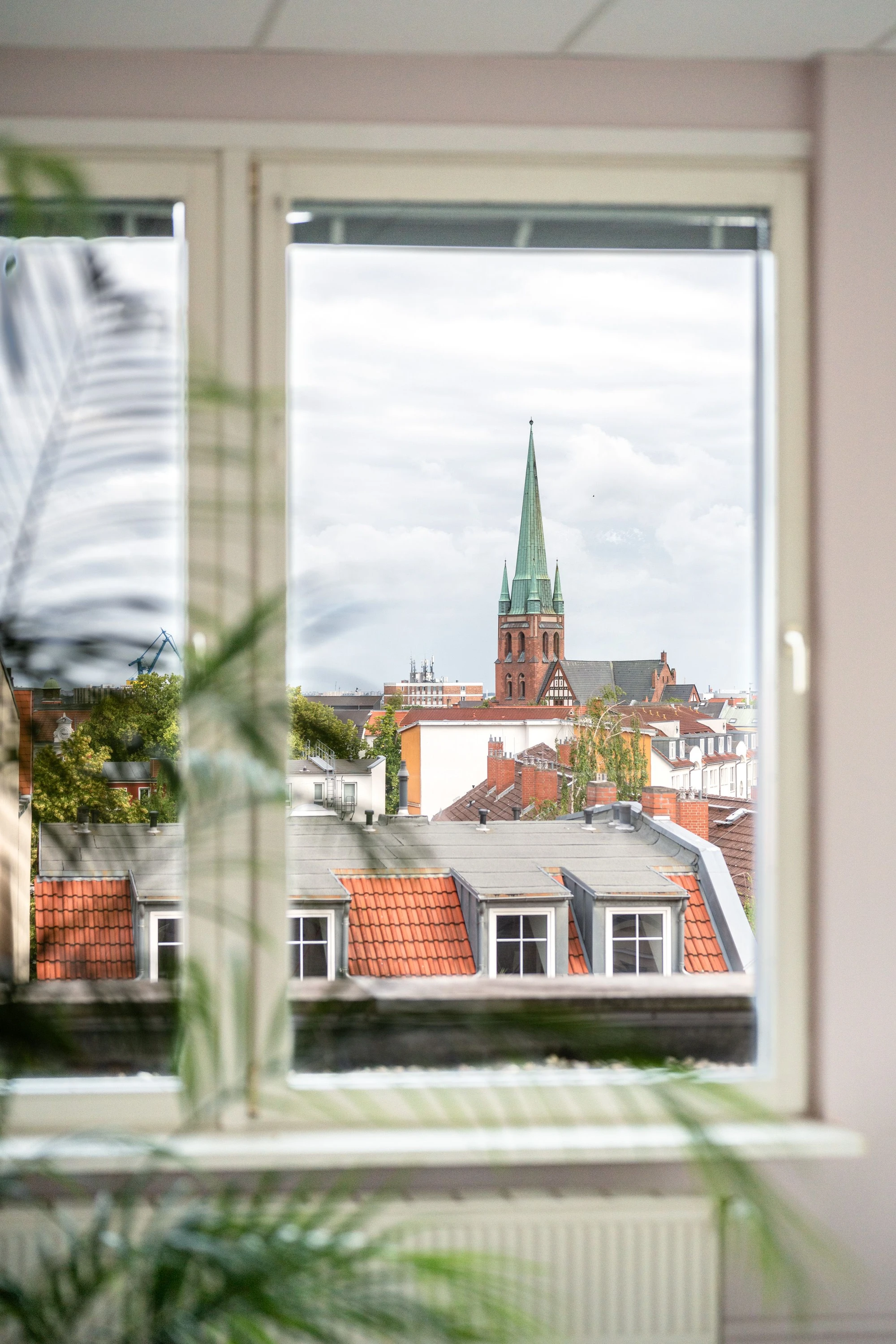 Blick aus einem Fenster auf eine Stadt mit einem markanten Kirchturm und roten Dächern.