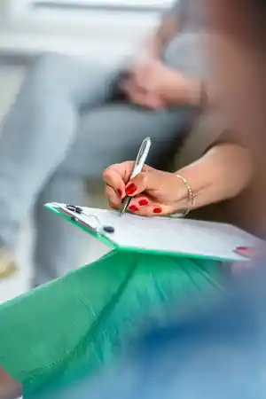 Eine Person mit rotem Nagellack schreibt mit einem Stift auf einem Clipboard.