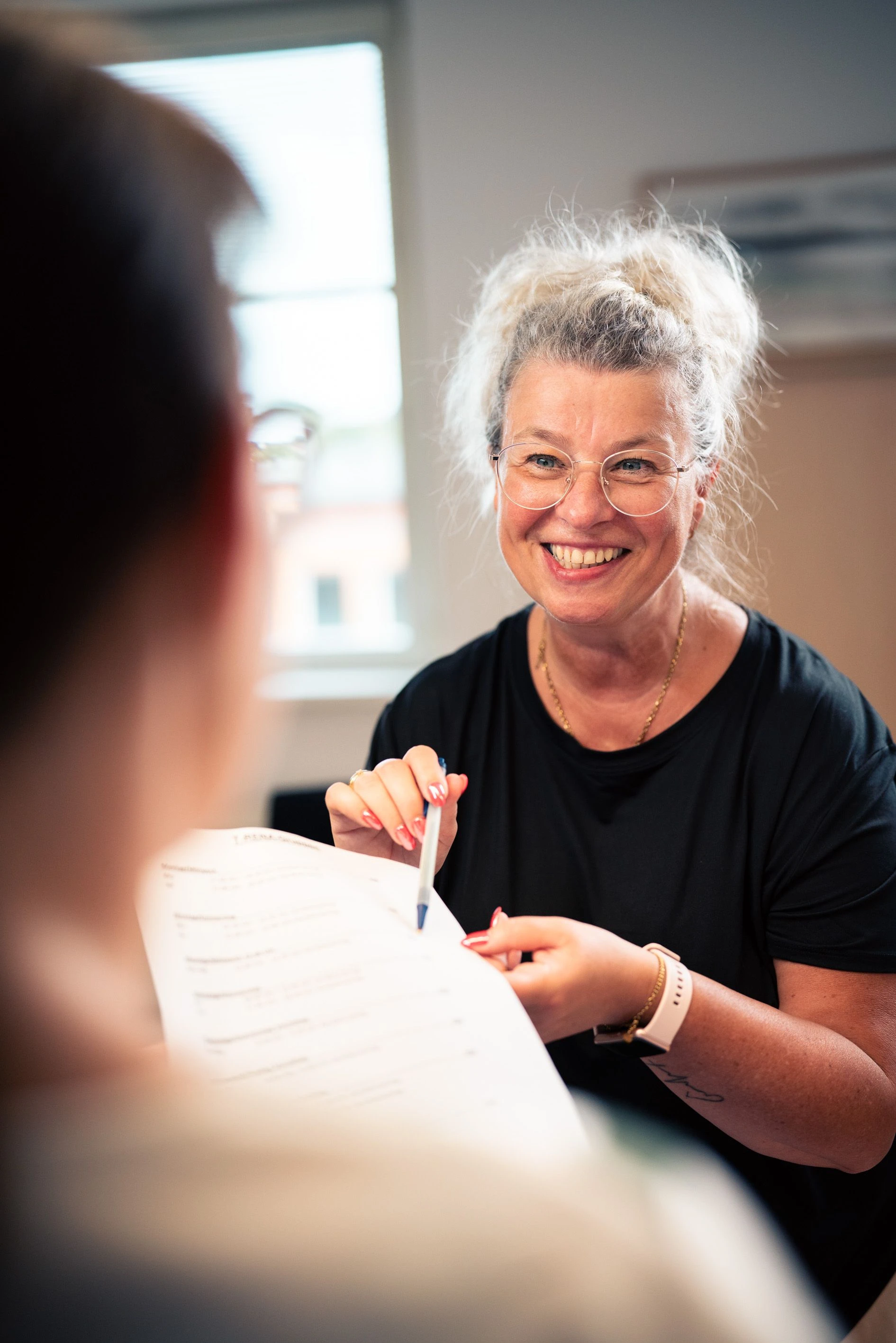 Eine lächelnde Frau erklärt etwas auf einem Dokument und hält einen Stift in der Hand.