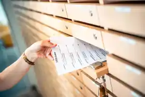 Eine Hand zieht ein Dokument aus einem Holzschrank mit mehreren Schubladen.