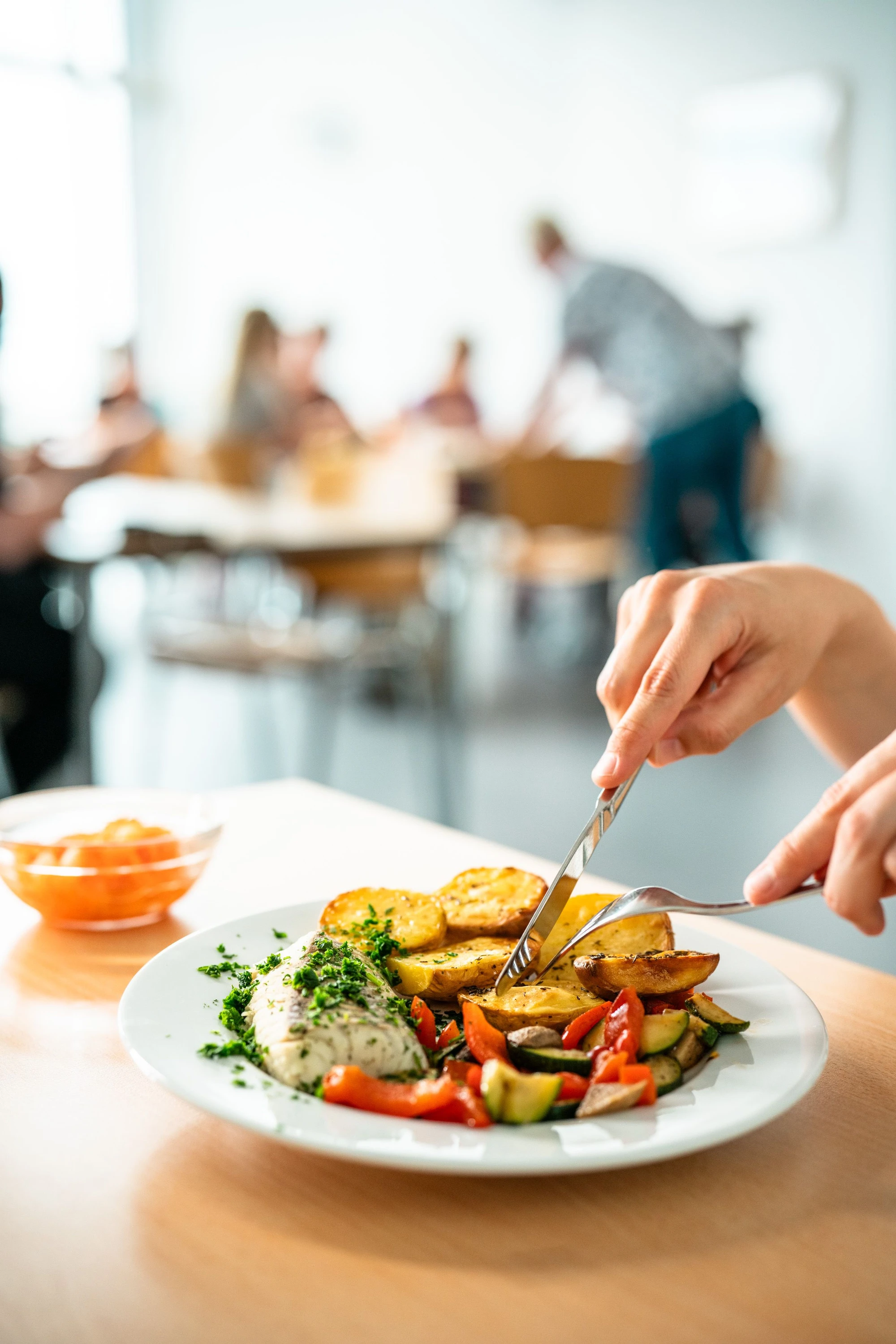 Eine Person schneidet ein Gericht mit Kartoffeln und Gemüse in einer Cafeteria.
