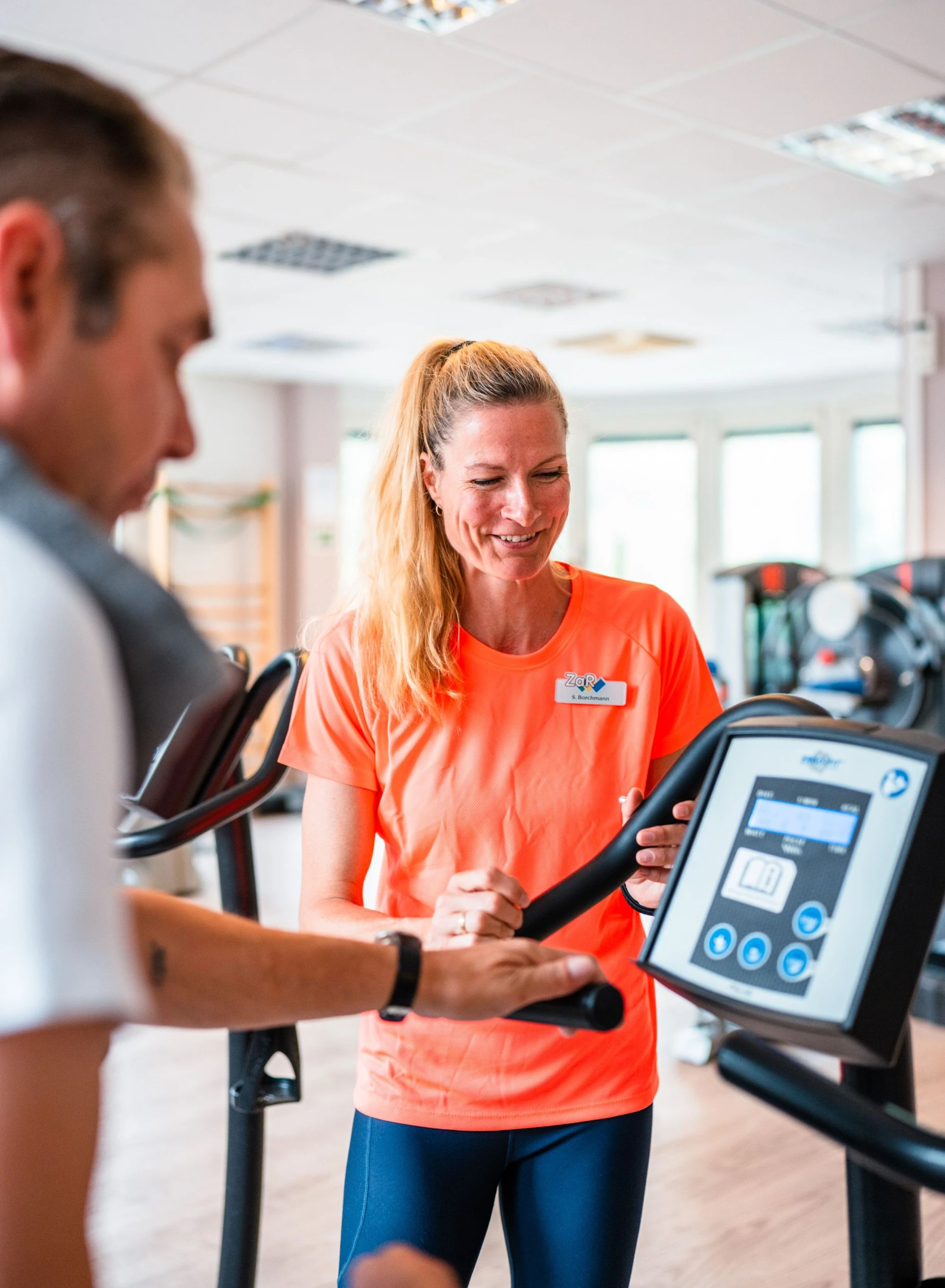 Eine Trainerin erklärt einem Mann die Nutzung eines Fitnessgeräts im Studio.