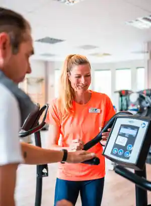 Eine Trainerin erklärt einem Mann die Nutzung eines Fitnessgeräts im Studio.