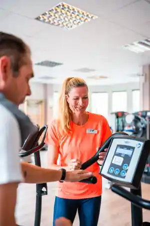 Eine Trainerin erklärt einem Mann die Nutzung eines Fitnessgeräts im Studio.