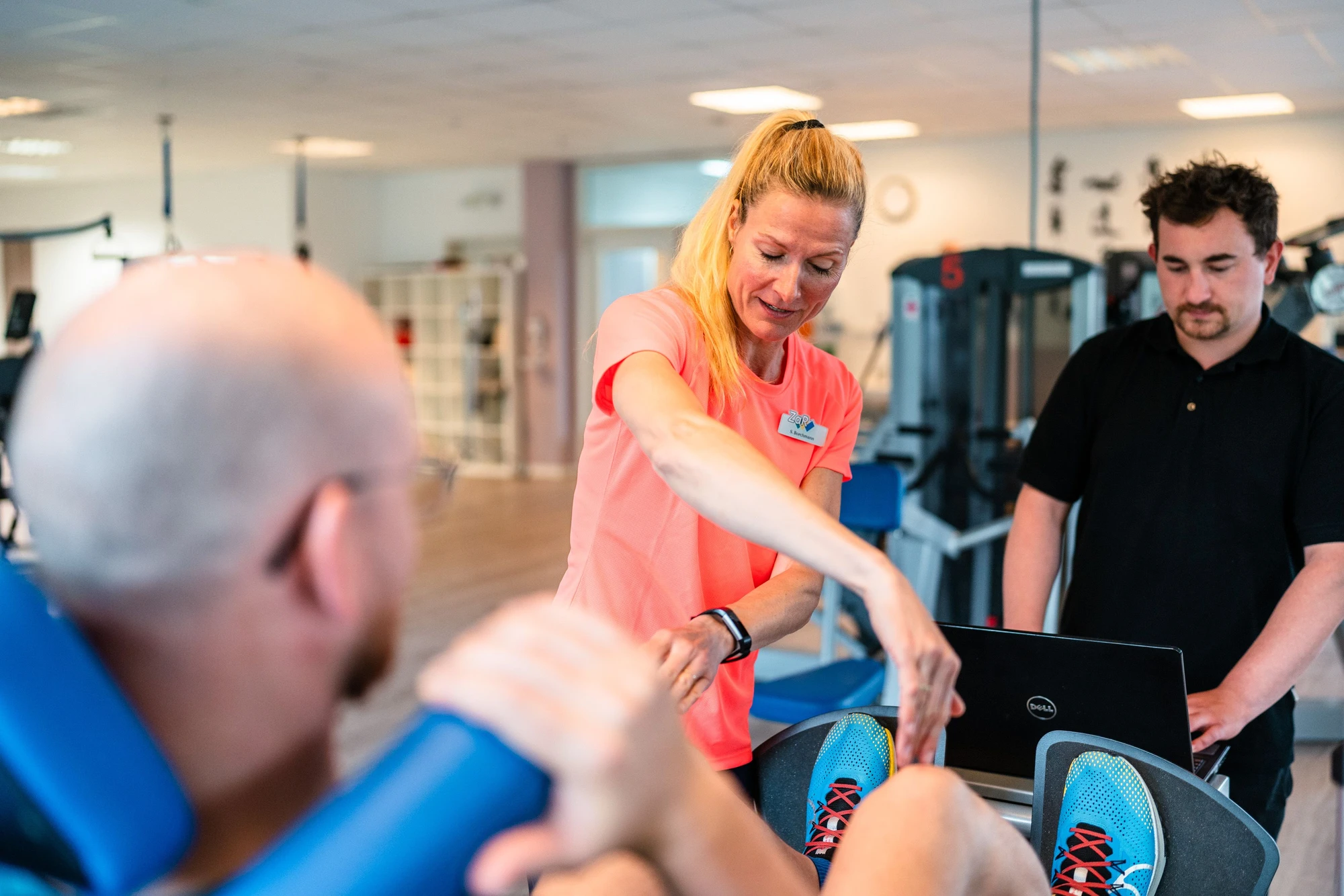 Trainerin erklärt Übungen an einem Fitnessgerät, während zwei Personen aufmerksam zuhören.