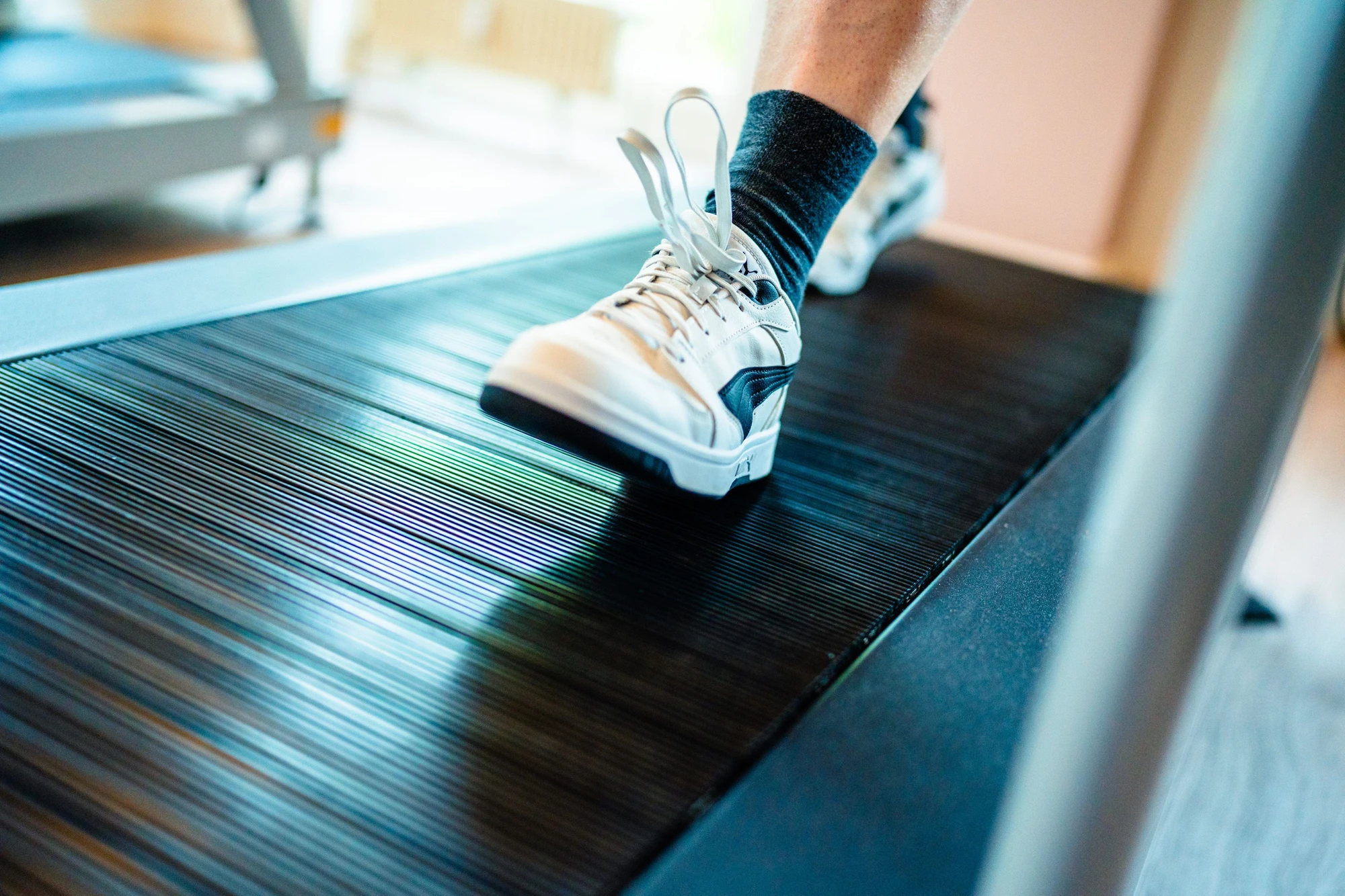 Ein Fuß in einem weißen Sportschuh läuft auf einem Laufband in einem Fitnessstudio.