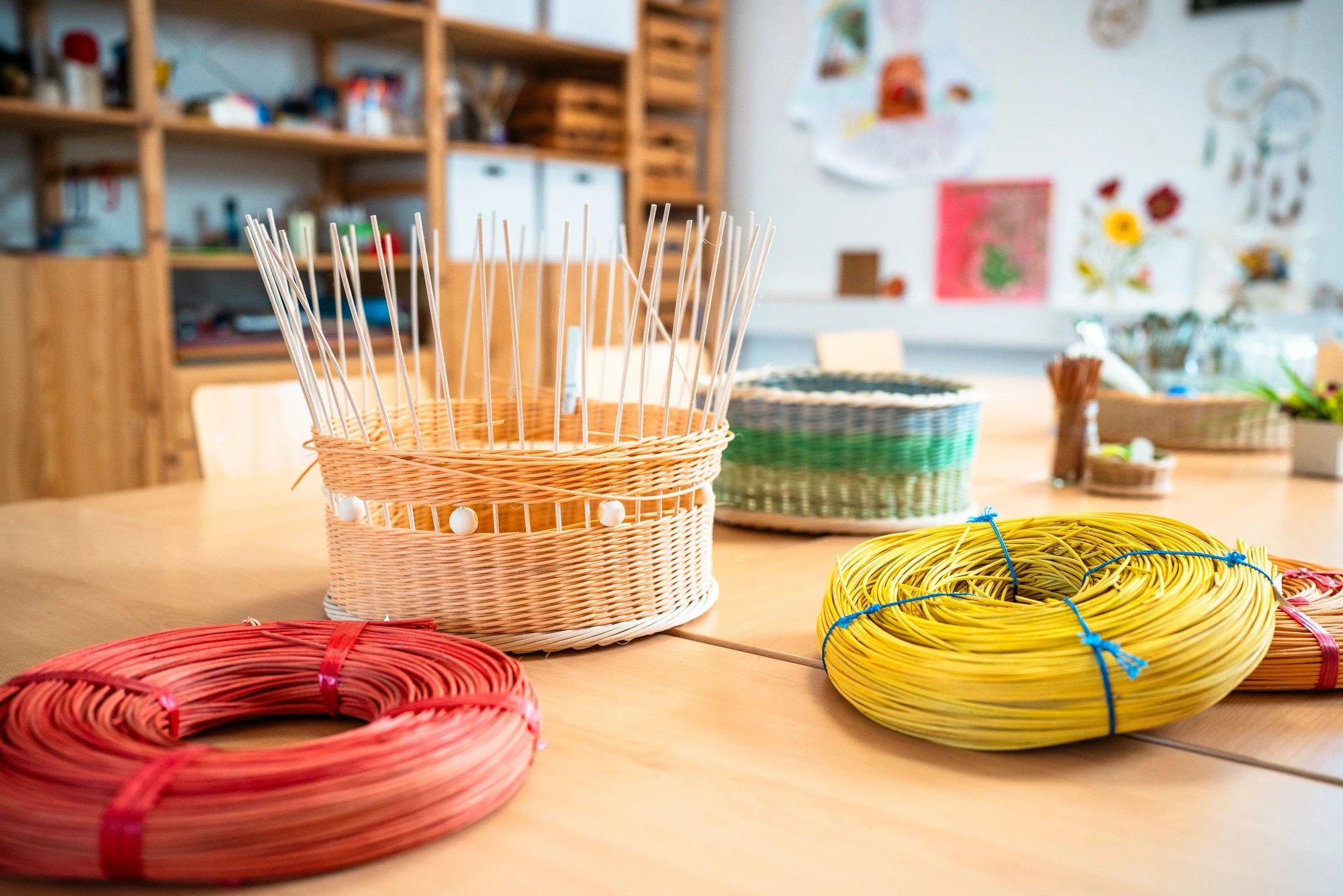 Bunte Bastelmaterialien auf einem Tisch, darunter Körbe und Drahtrollen in verschiedenen Farben.