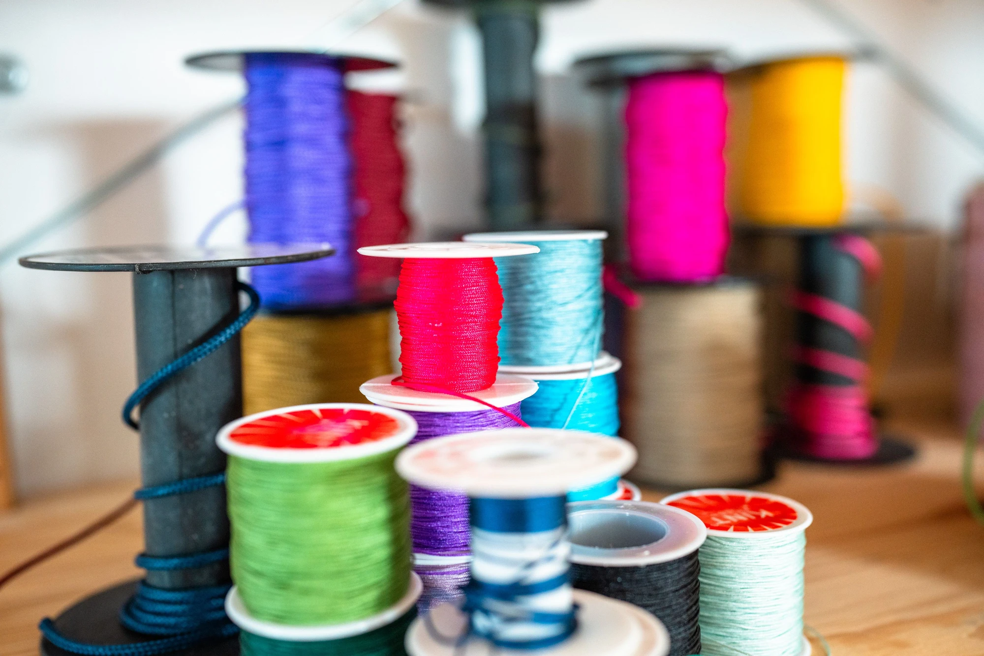 Bunte Garnrollen auf Spulen, ordentlich gestapelt in einem kreativen Arbeitsbereich.