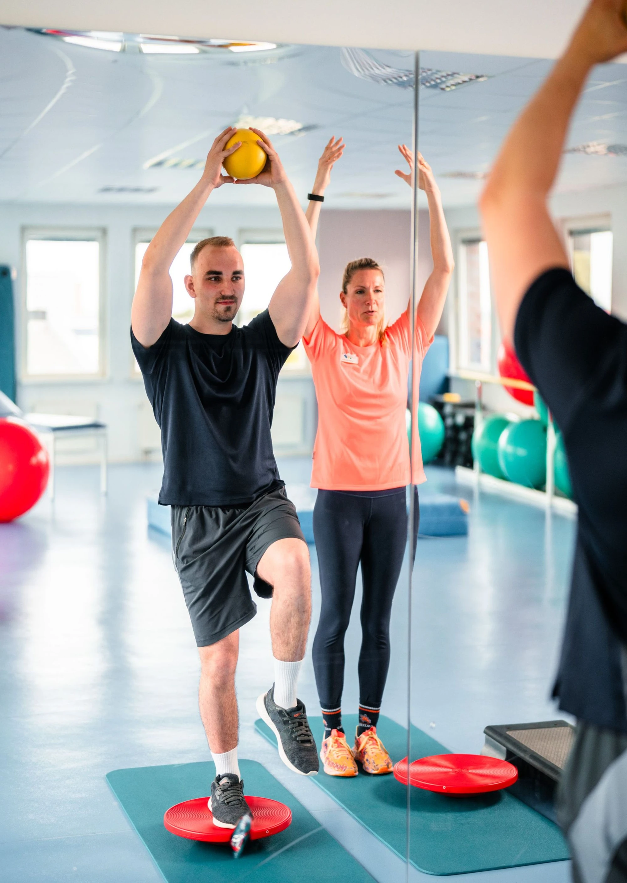 Zwei Personen trainieren in einem Fitnessraum mit einem Medizinball und Balance-Boards.
