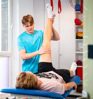 Ein junger Mann dehnt das Bein eines anderen Mannes während einer physiotherapeutischen Behandlung.