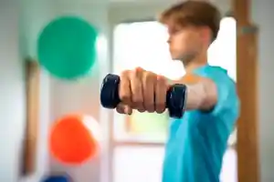 Ein Junge hält eine Hantel in der Hand und trainiert in einem hellen Raum.