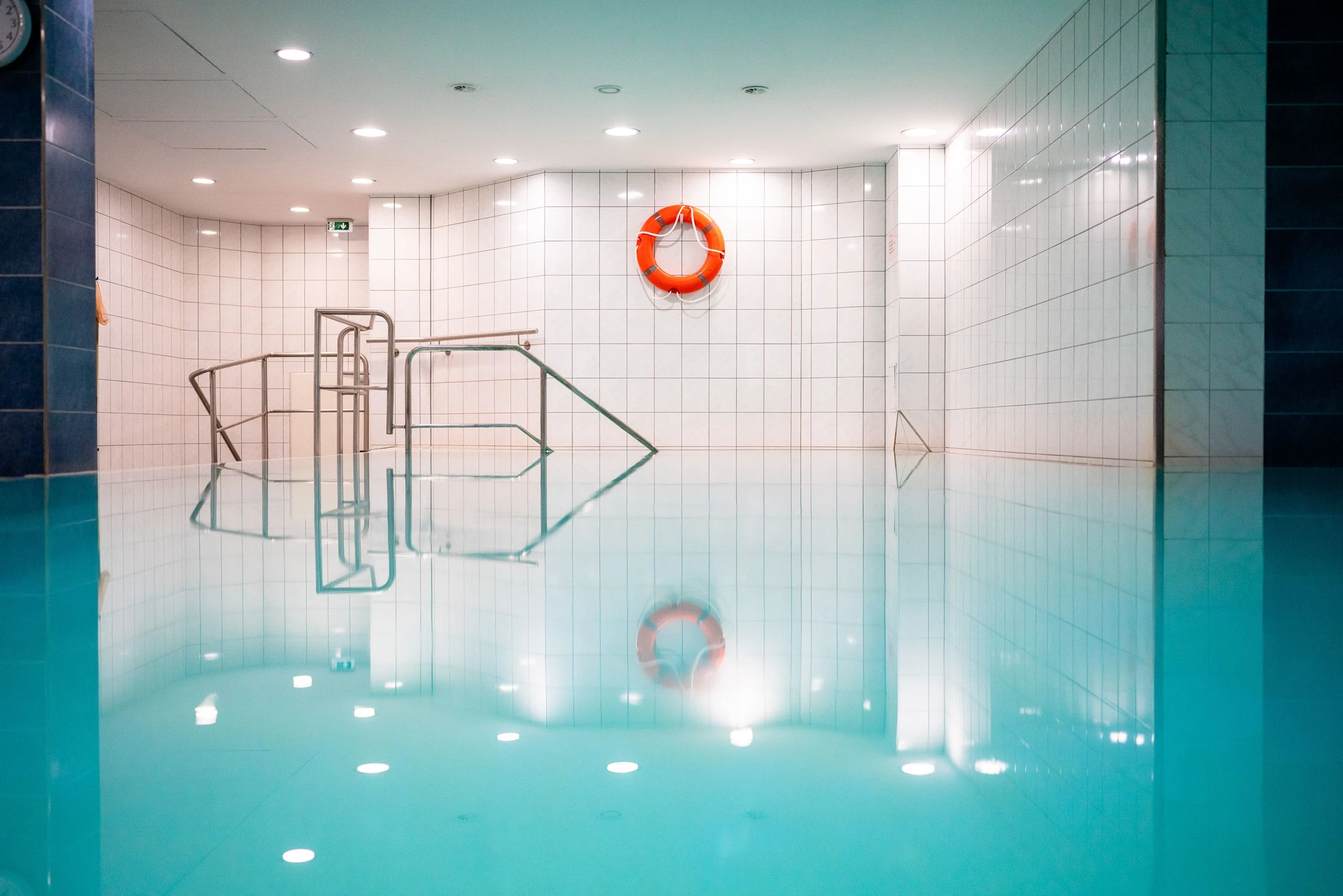 Leerer Schwimmbereich mit blauer Wasseroberfläche und orangefarbener Rettungsringwand.